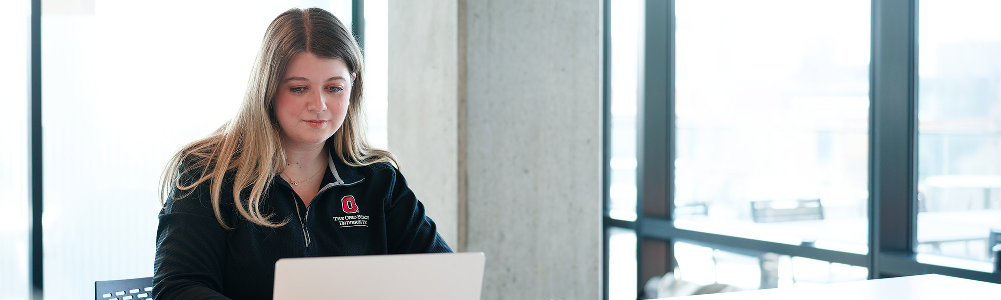 Female professional in an Ohio State sweatshirt continues her education online from her laptop.