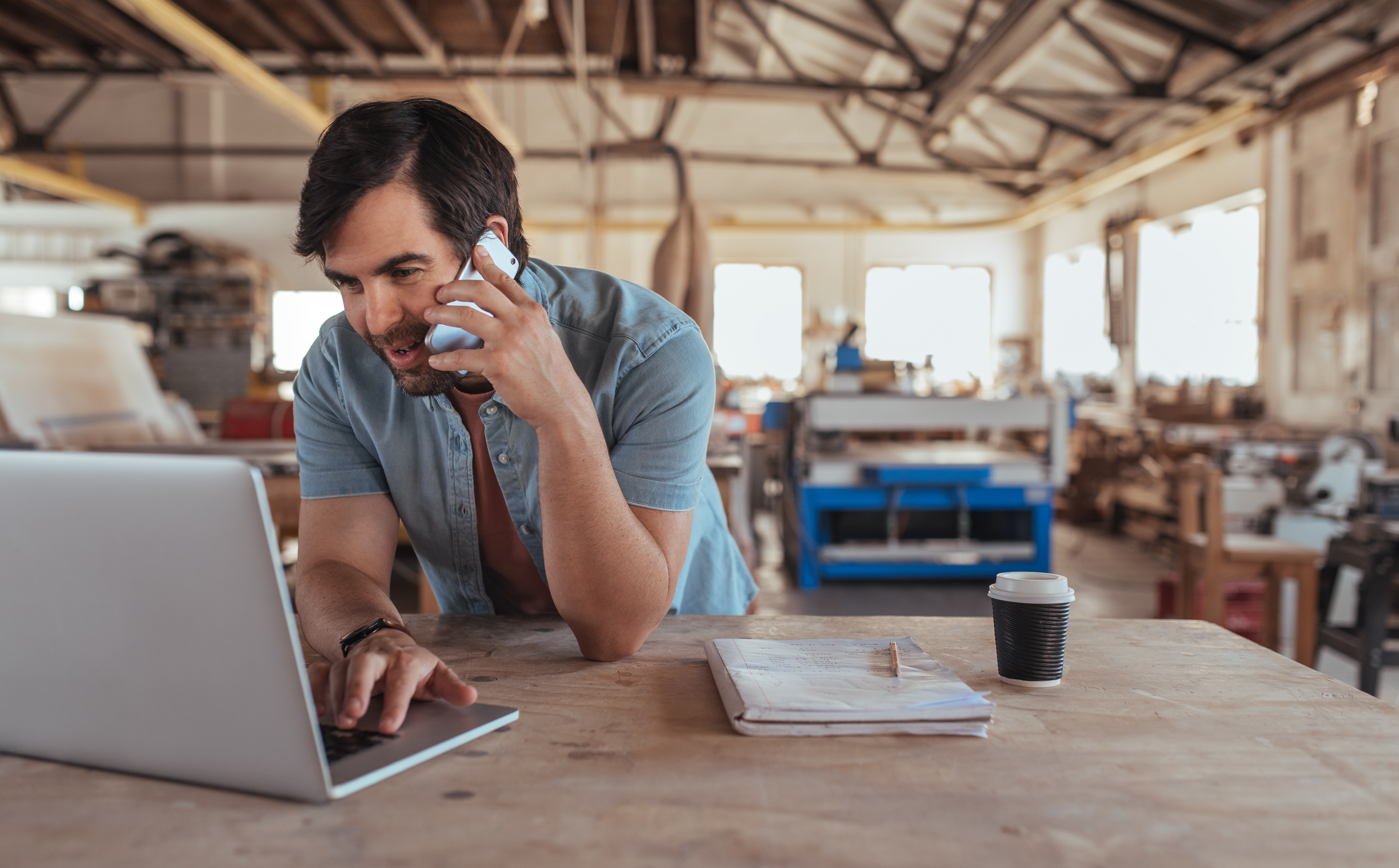 A business owner smiles as he works on his laptop during a phone call.