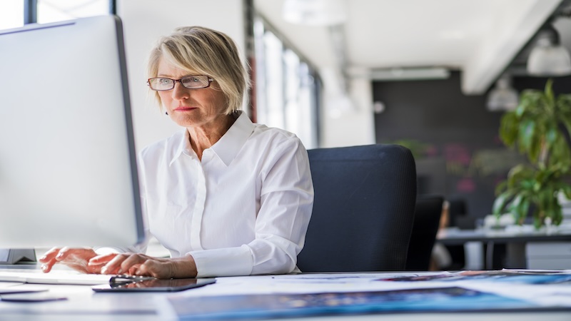 An older businesswoman at her desk focusing on a computer screen